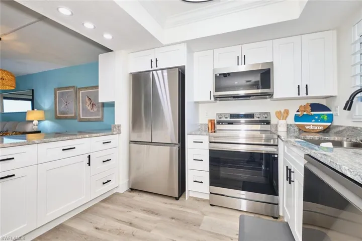 Kitchen featuring stainless steel appliances, white cabinetry, light stone countertops, light wood finished floors, and recessed lighting