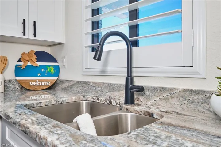 Kitchen view of white cabinetry, light stone countertops, and a textured wall