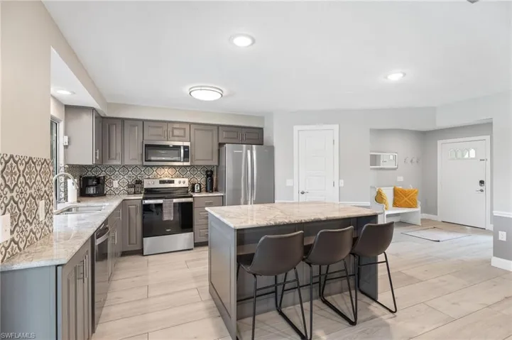 Kitchen with appliances with stainless steel finishes, a kitchen island, light stone countertops, gray cabinets, and sink
