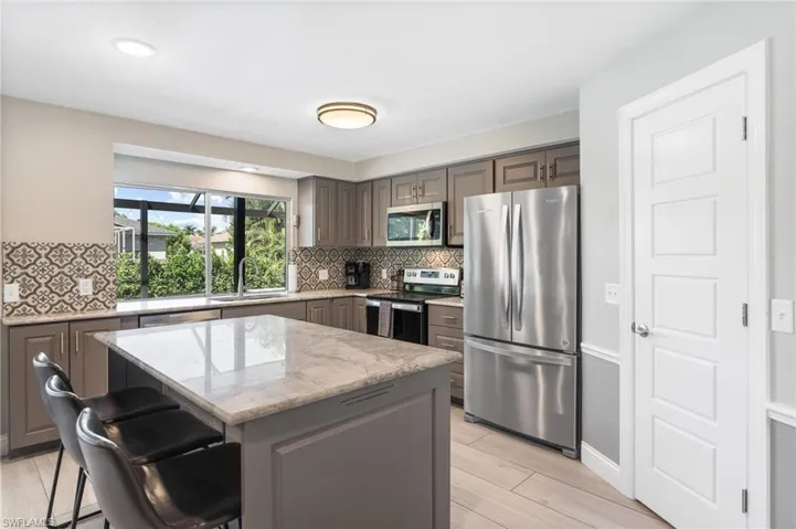 Kitchen with appliances with stainless steel finishes, decorative backsplash, a breakfast bar, a kitchen island, and light tile flooring