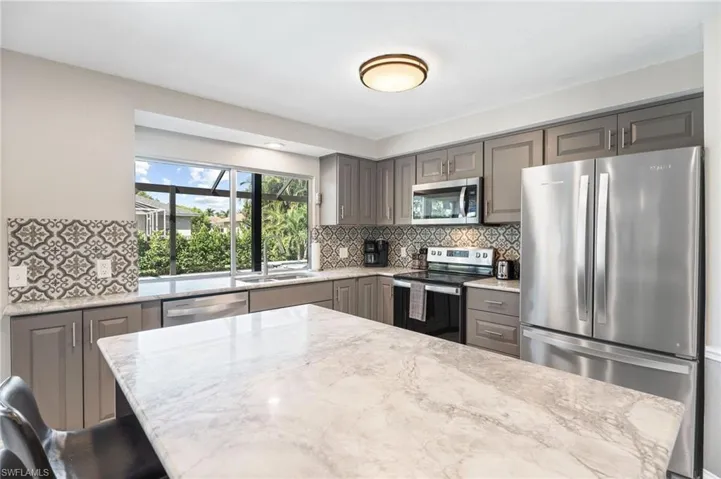 Kitchen featuring appliances with stainless steel finishes, backsplash, light stone countertops, a breakfast bar area, and sink