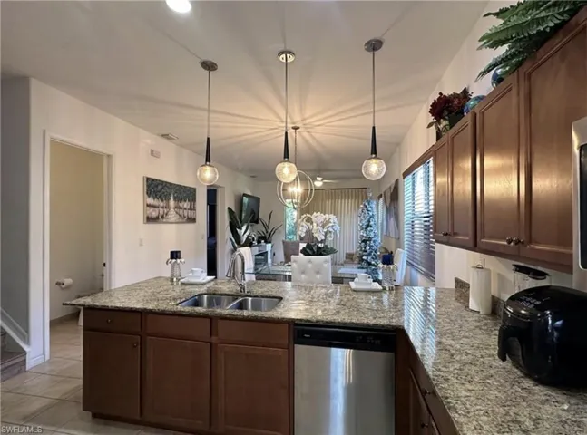 Kitchen with a peninsula, stainless steel dishwasher, pendant lighting, light stone countertops, and light tile patterned flooring