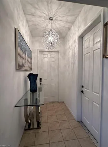 Hall with light tile patterned flooring and a chandelier