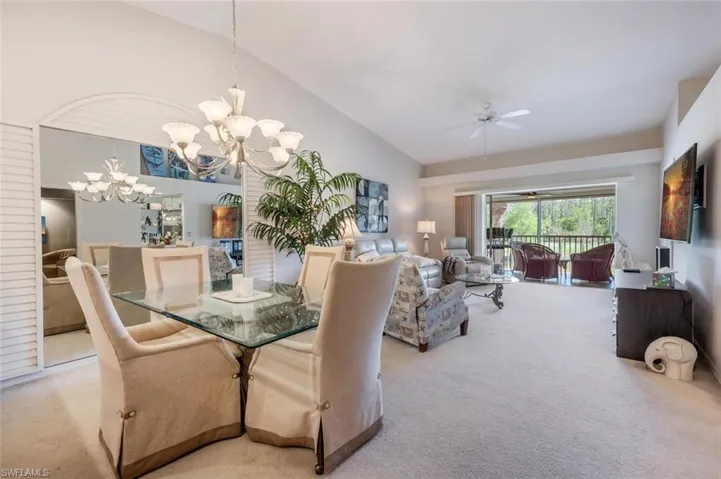 Carpeted dining room featuring ceiling fan with notable chandelier and high vaulted ceiling