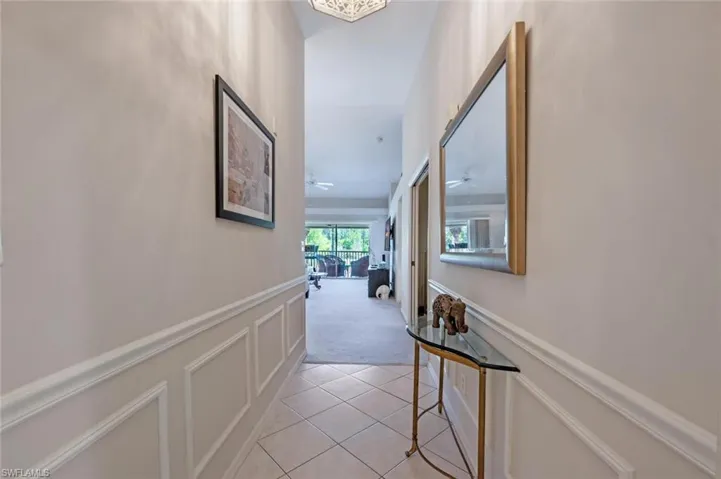 Corridor featuring a decorative wall, light tile patterned flooring, light colored carpet, and wainscoting