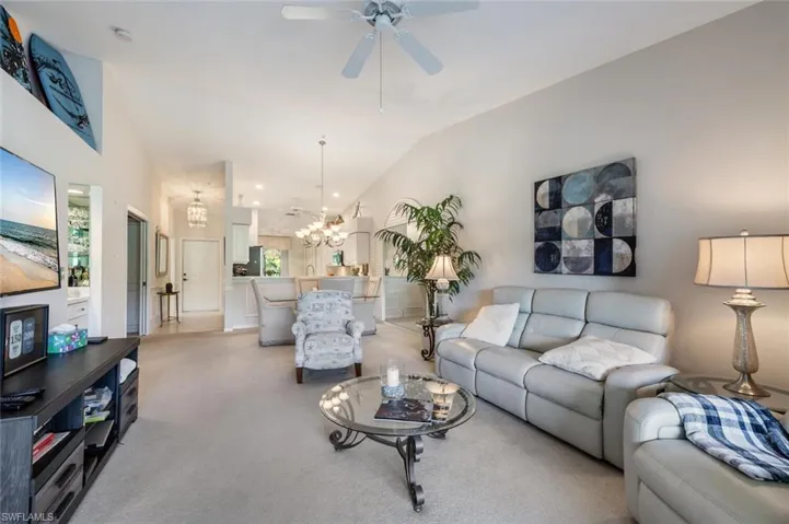 Living room with light colored carpet, lofted ceiling, and ceiling fan with notable chandelier