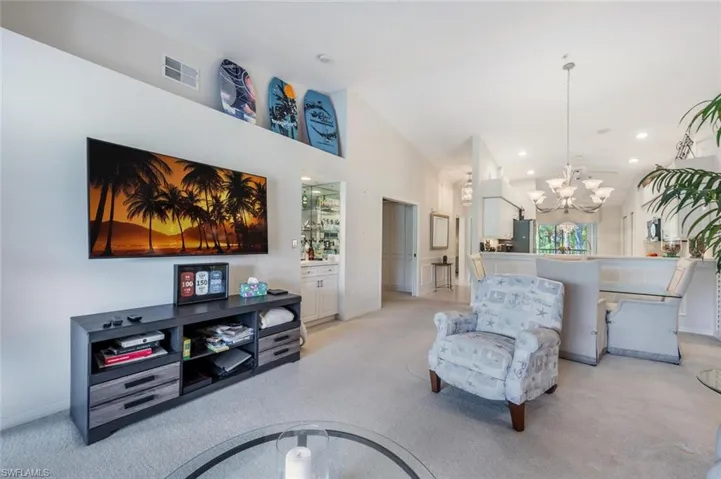 Living area featuring an inviting chandelier, high vaulted ceiling, light colored carpet, and visible vents