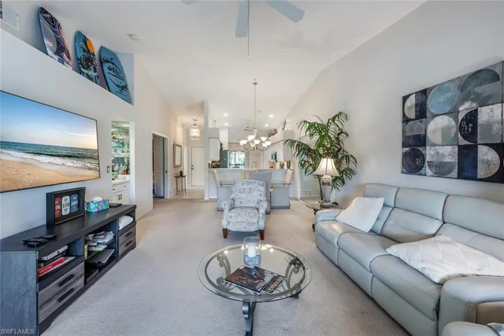 Living room with high vaulted ceiling, visible vents, ceiling fan with notable chandelier, and light carpet