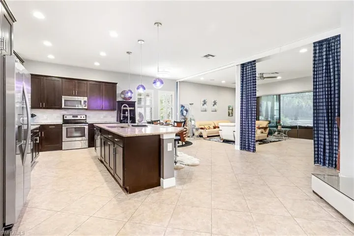 Kitchen featuring appliances with stainless steel finishes, pendant lighting, open floor plan, light stone counters, and dark brown cabinets