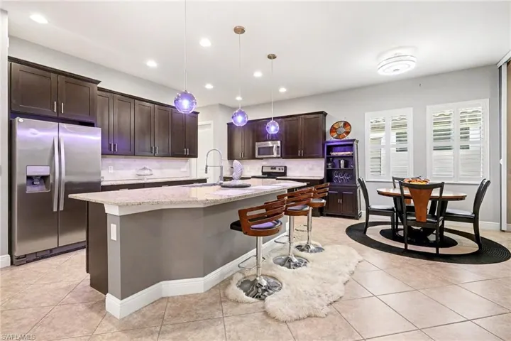 Kitchen with a kitchen breakfast bar, stainless steel appliances, dark brown cabinets, pendant lighting, and an island with sink