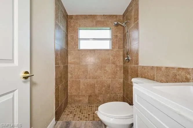 Bathroom featuring hardwood / wood-style floors, vanity, tiled shower, and toilet