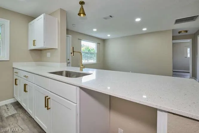 Kitchen with light hardwood / wood-style flooring, sink, light stone counters, and white cabinetry