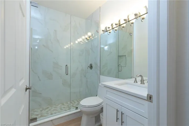 Downstairs bathroom with vanity, a marble finish shower, and light wood-style  finished floors
