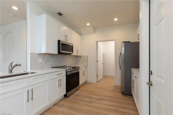 Kitchen featuring stainless steel appliances, white cabinetry, tasteful backsplash, light countertops, and light wood-style floors