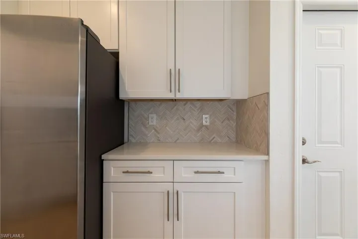 Kitchen featuring freestanding refrigerator, decorative backsplash, light countertops, and white cabinets