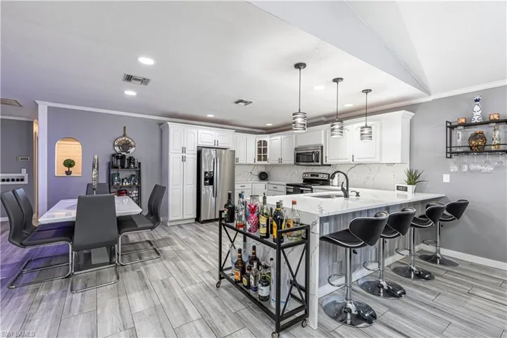 Kitchen with crown molding, a kitchen breakfast bar, stainless steel appliances, a peninsula, and light stone countertops