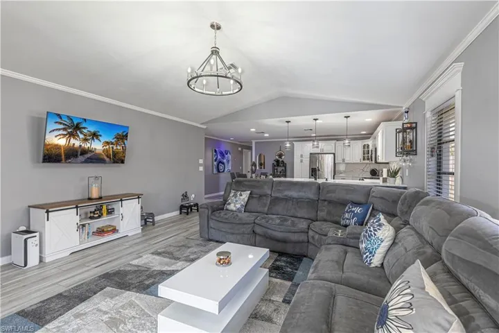 Living area featuring crown molding, lofted ceiling, wood finished floors, and a chandelier