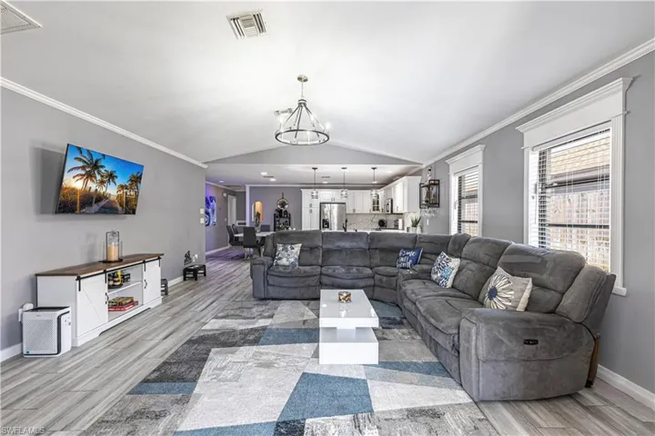 Living room featuring crown molding, lofted ceiling, wood tiled floors, and a chandelier