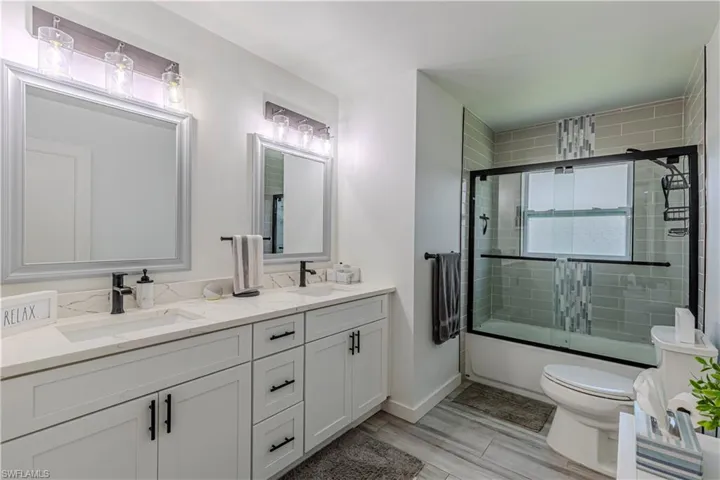Full bathroom featuring double vanity, combined bath / shower with glass door, and wood tiled floors