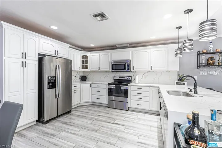 Kitchen with stainless steel appliances, hanging light fixtures, light stone counters, recessed lighting, and white cabinets