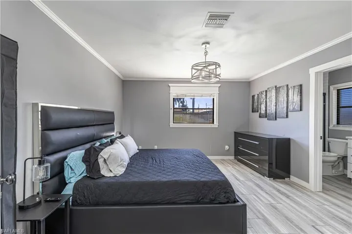 Bedroom with wood tiled floors, ornamental molding, and connected bathroom