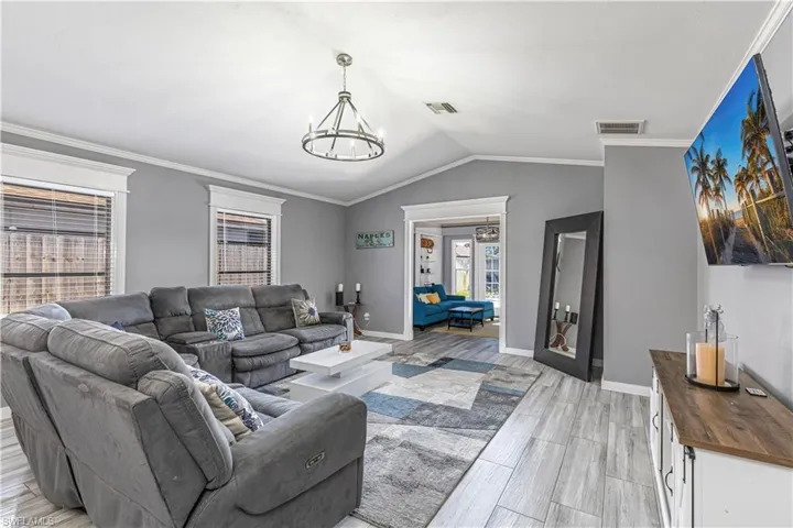 Living area with crown molding, vaulted ceiling, a chandelier, wood tiled floors, and french doors