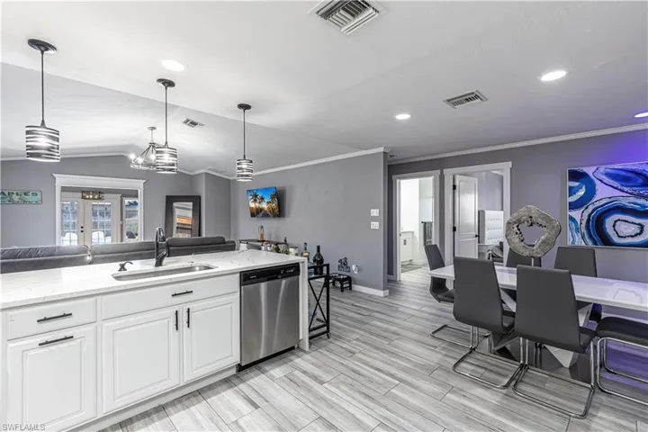 Kitchen featuring open floor plan, white cabinets, decorative light fixtures, light stone counters, and stainless steel dishwasher