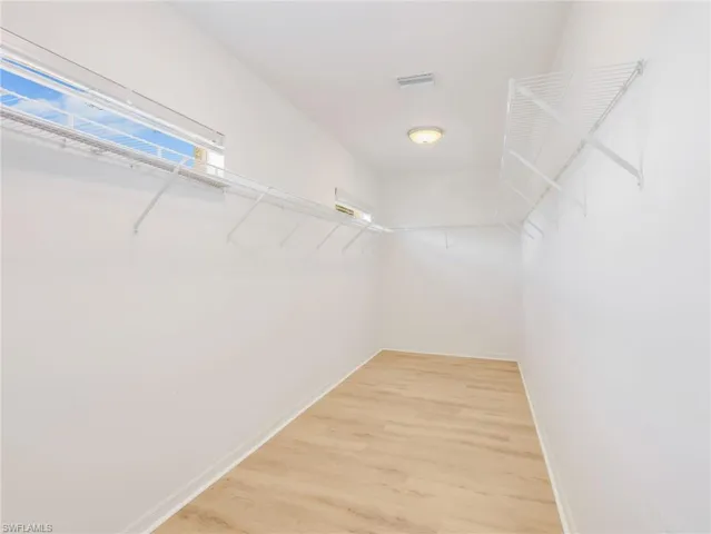 Spacious walk-in closet featuring light wood-finish flooring, white walls, and built-in wire shelving