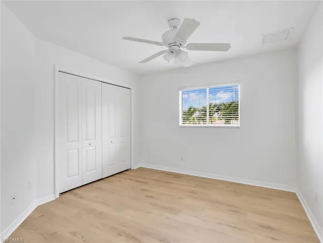 Interior room with wood-finish flooring, white walls, and a white ceiling fan with integrated lighting