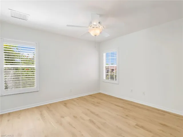 Bright room featuring wood-finish flooring, white walls, and a ceiling fan with integrated lighting