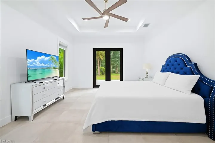 Bedroom with a tray ceiling, light tile patterned floors, and ceiling fan
