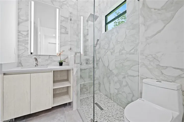Bathroom with tile walls, a marble finish shower, and vanity