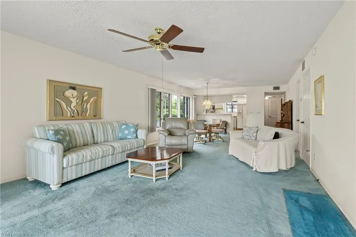 Carpeted living room with ceiling fan and a textured ceiling