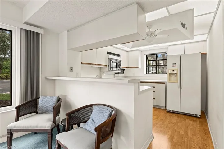 Kitchen with ceiling fan, kitchen peninsula, plenty of natural light, white refrigerator with ice dispenser, and white cabinets