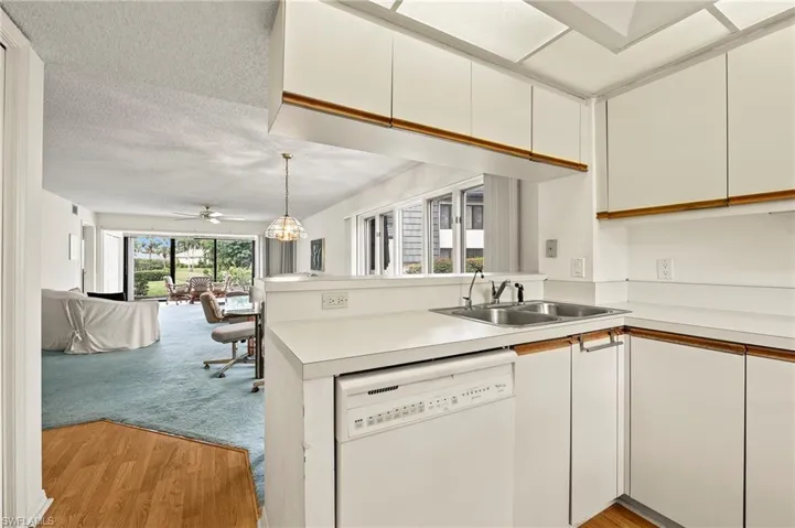 Kitchen with dishwasher, kitchen peninsula, sink, white cabinetry, and light carpet