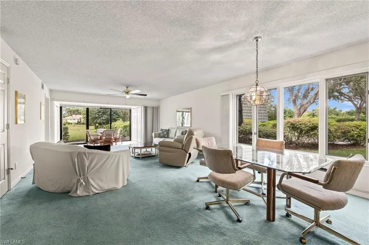 Carpeted dining space featuring a textured ceiling, a healthy amount of sunlight, and ceiling fan with notable chandelier
