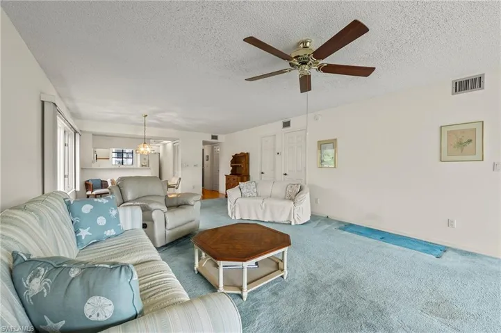 Carpeted living room featuring ceiling fan with notable chandelier and a textured ceiling