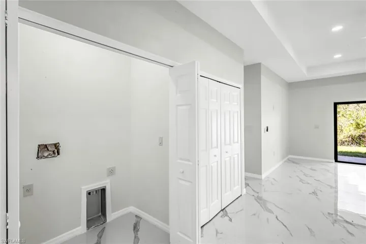 Laundry area with recessed lighting, electric dryer hookup, a raised ceiling, and light marble finish floors