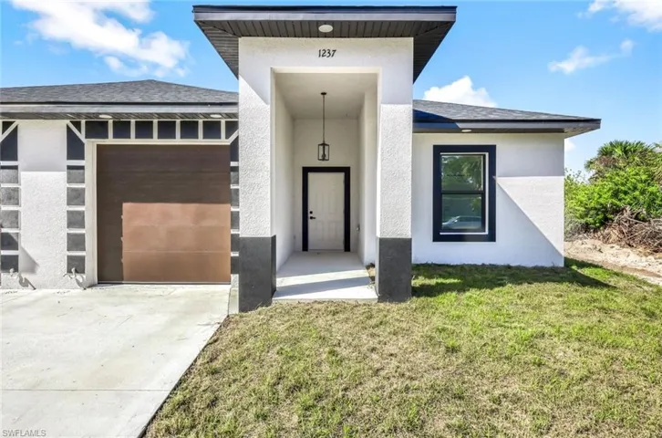Doorway to property featuring an attached garage, a yard, concrete driveway, roof with shingles, and stucco siding