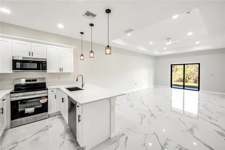 Kitchen featuring stainless steel appliances, open floor plan, a peninsula, white cabinetry, and a raised ceiling