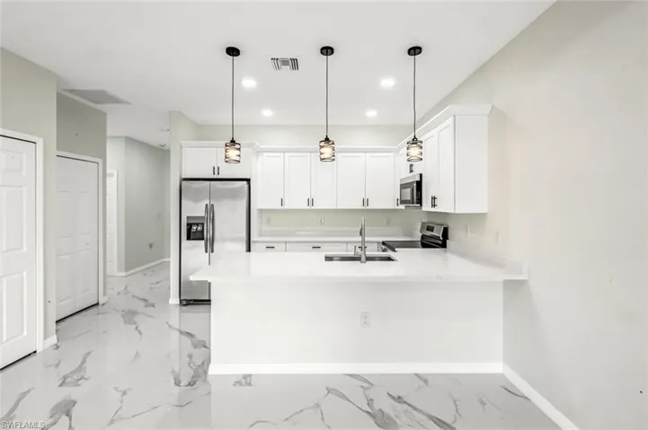 Kitchen featuring a peninsula, stainless steel appliances, white cabinetry, light stone counters, and decorative light fixtures
