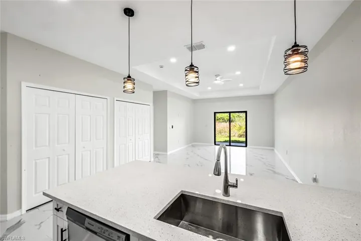 Kitchen featuring light stone countertops, stainless steel dishwasher, light marble finish floors, and a raised ceiling