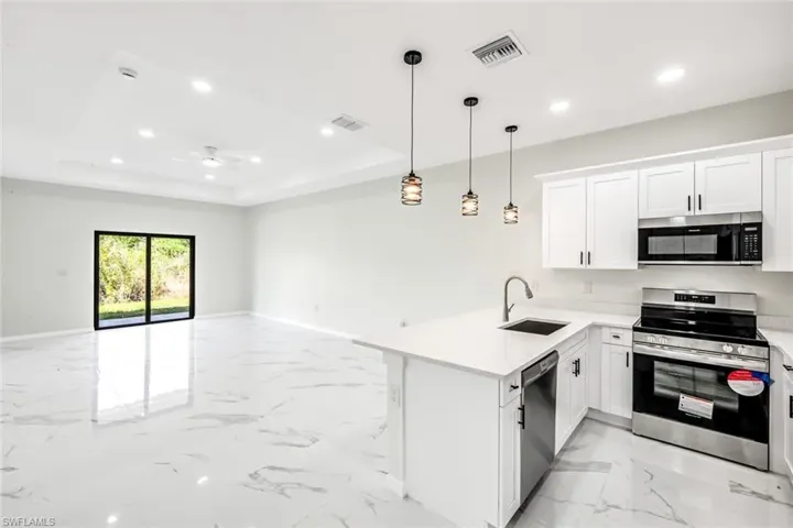 Kitchen featuring stainless steel appliances, white cabinets, open floor plan, a peninsula, and light stone countertops