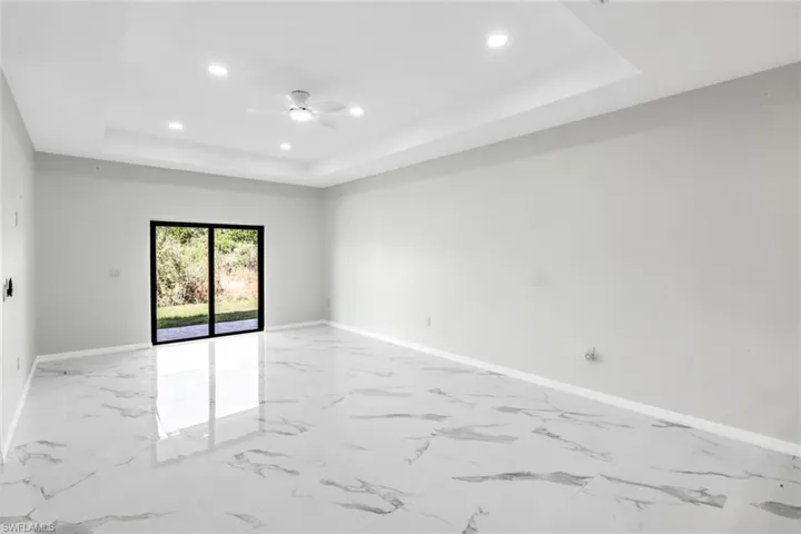 Unfurnished room with recessed lighting, a ceiling fan, light marble finish floors, and a tray ceiling