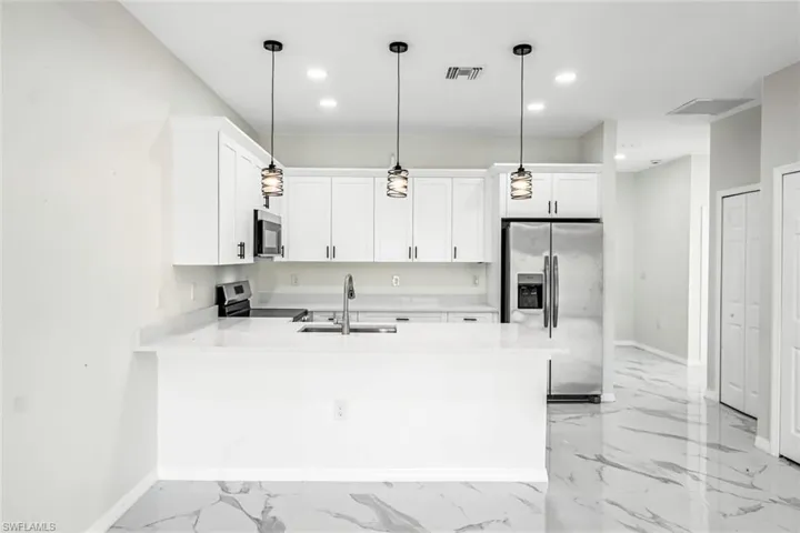 Kitchen with stainless steel appliances, a peninsula, light stone counters, white cabinets, and decorative light fixtures