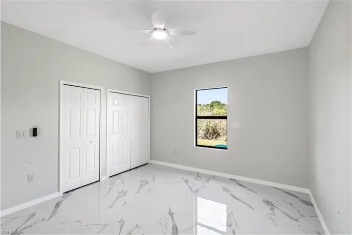 Unfurnished bedroom featuring two closets, ceiling fan, and light marble finish floors
