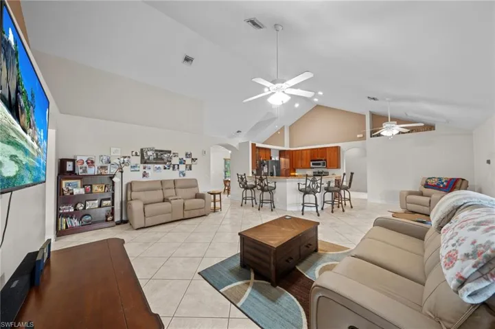 Living room featuring arched walkways, light tile patterned floors, high vaulted ceiling, and ceiling fan
