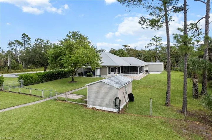 Rear view of house with a lawn, a sunroom, an outdoor structure, and view of scattered trees
