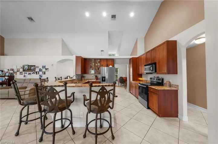 Kitchen with appliances with stainless steel finishes, a peninsula, brown cabinets, a breakfast bar, and high vaulted ceiling