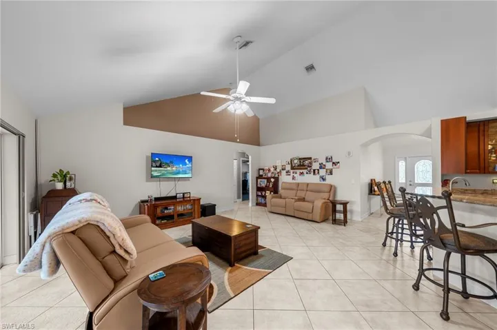 Living room featuring arched walkways, high vaulted ceiling, light tile patterned floors, and a ceiling fan